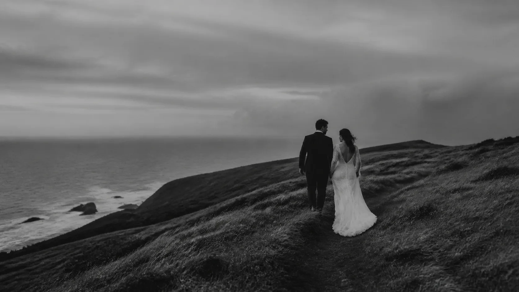 Newlyweds walking along a windswept coast